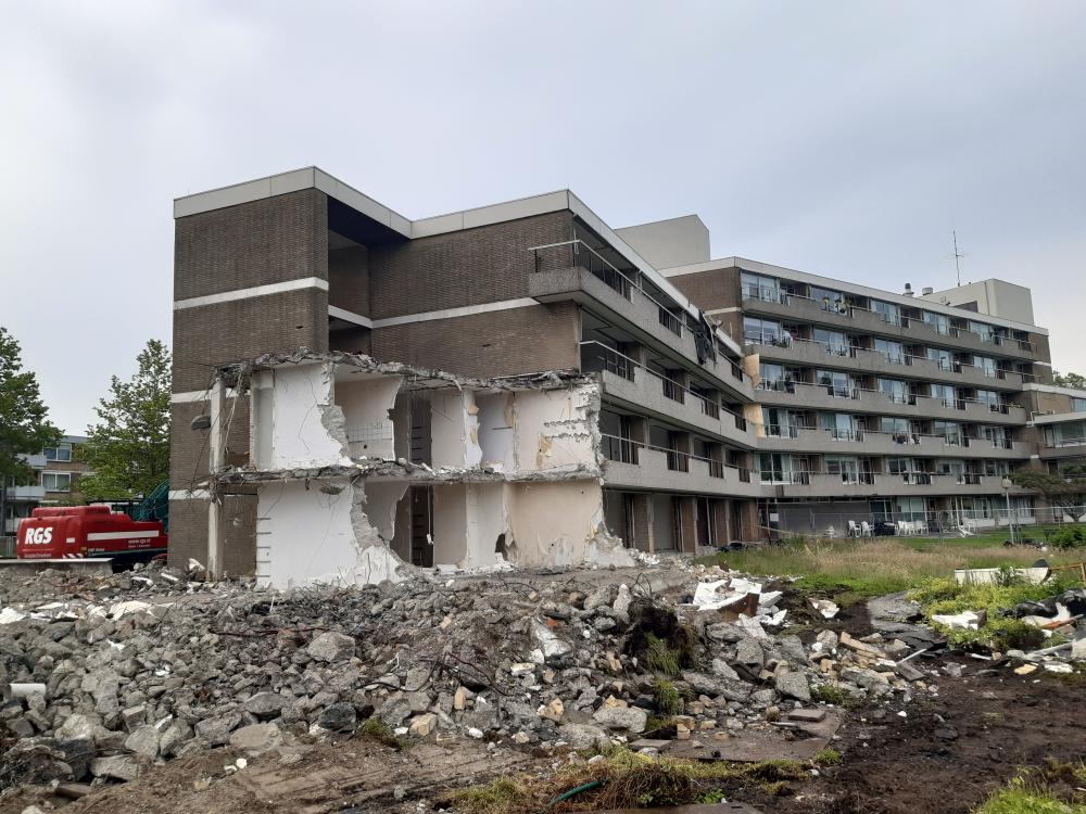 Afbeelding van een gedeeltelijk gesloopt gebouw met puin op de voorgrond en een grauwe lucht erboven.