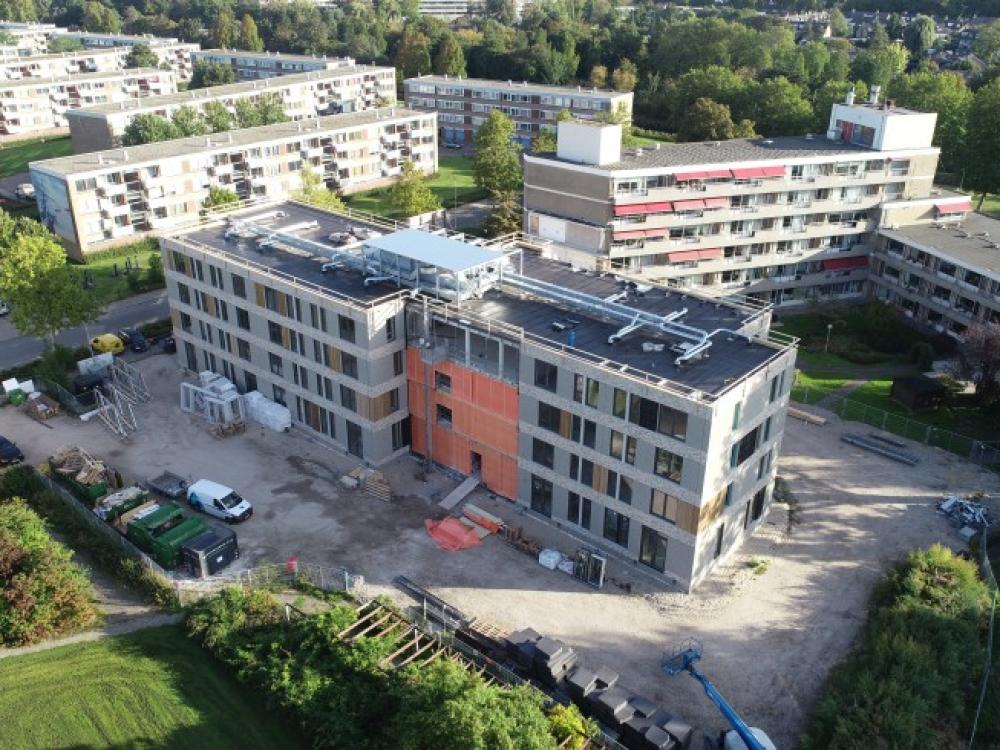 Luchtfoto van een bouwplaats met een bijna voltooid gebouw, omringd door groen en andere wooncomplexen op de achtergrond.