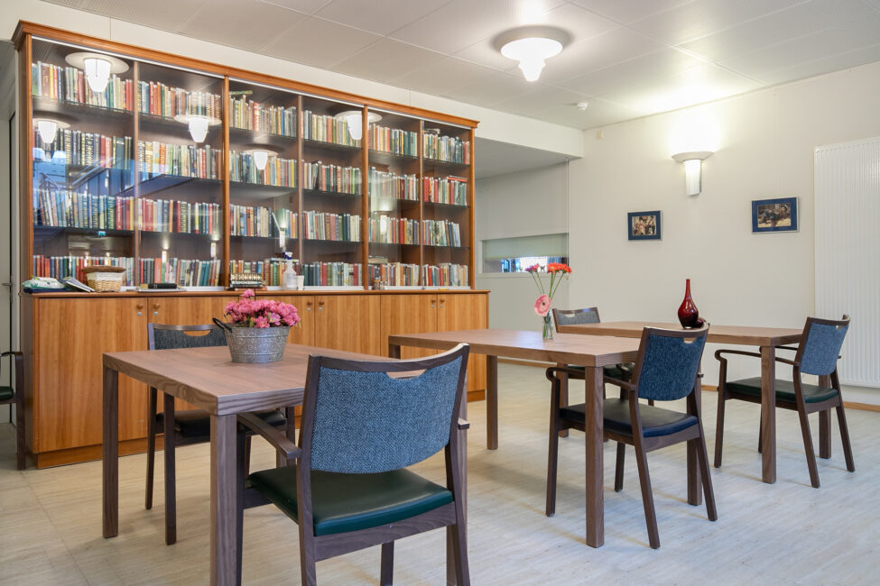 Een gezellige leesruimte met houten tafels en stoelen, een boekenkast vol boeken en bloemen op de tafels voor decoratie.