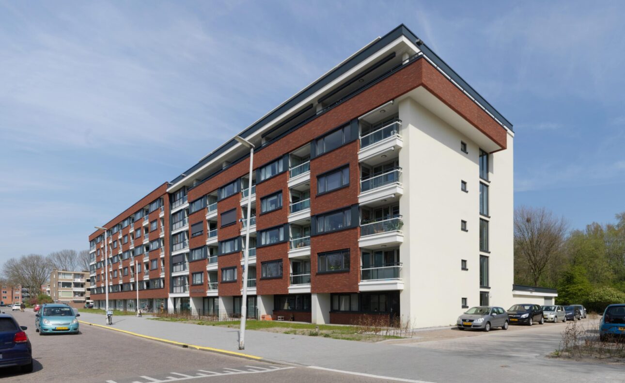 Afbeelding van een modern, vijf verdiepingen hoog appartementencomplex met balkons, gelegen aan een rustige straat.
