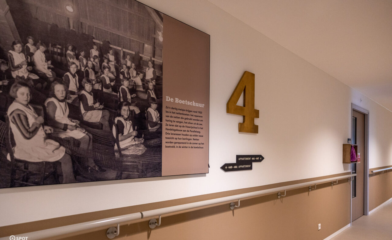 Een gang in een gebouw met een grote foto aan de muur en het nummer 4. De gang heeft een bruine en witte kleurstelling.