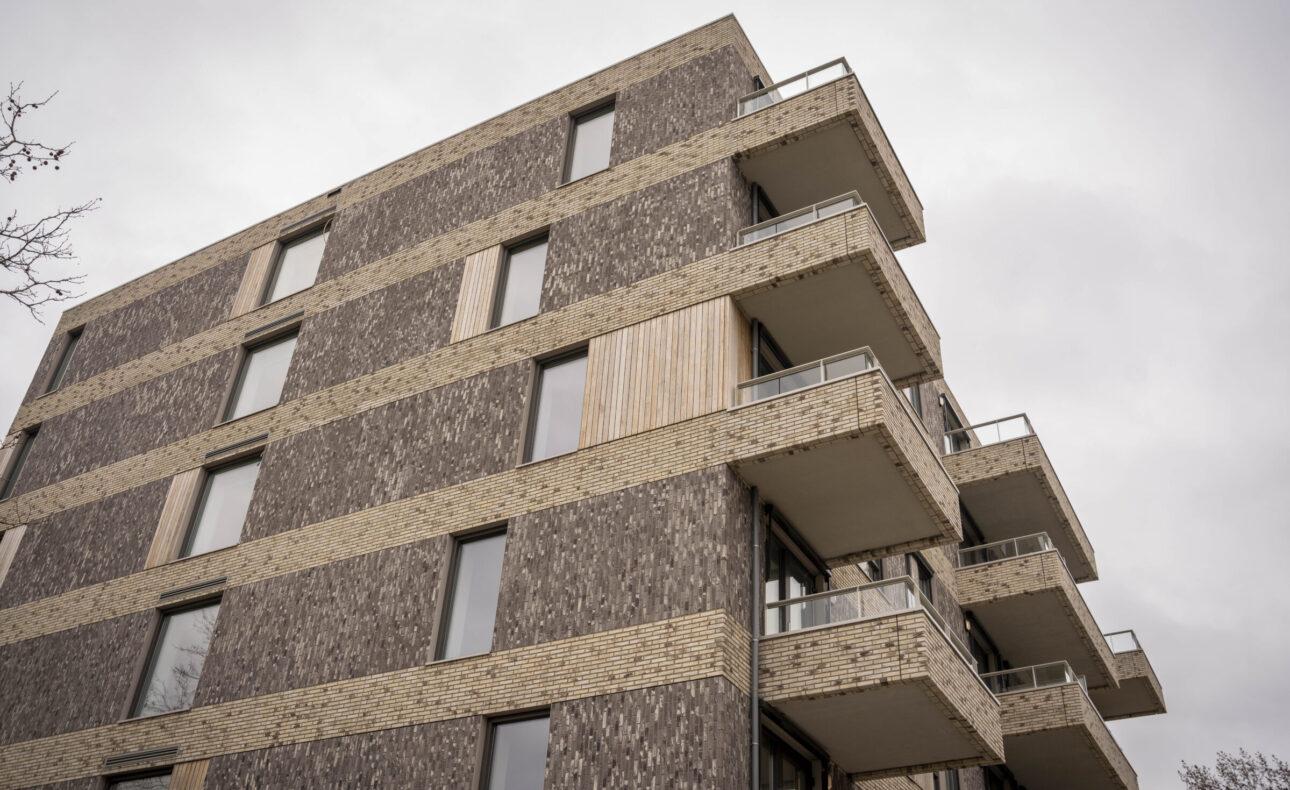 Buitenaanzicht van een modern appartementencomplex met meerdere verdiepingen en balkons, tegen een grijze lucht.