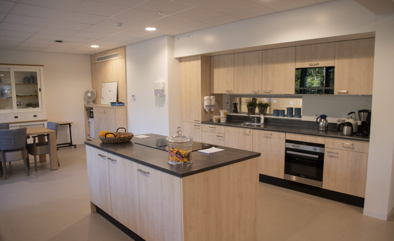 Moderne keuken met houten kasten, een kookeiland, en diverse apparaten. Op het eiland staat een schaal met fruit.
