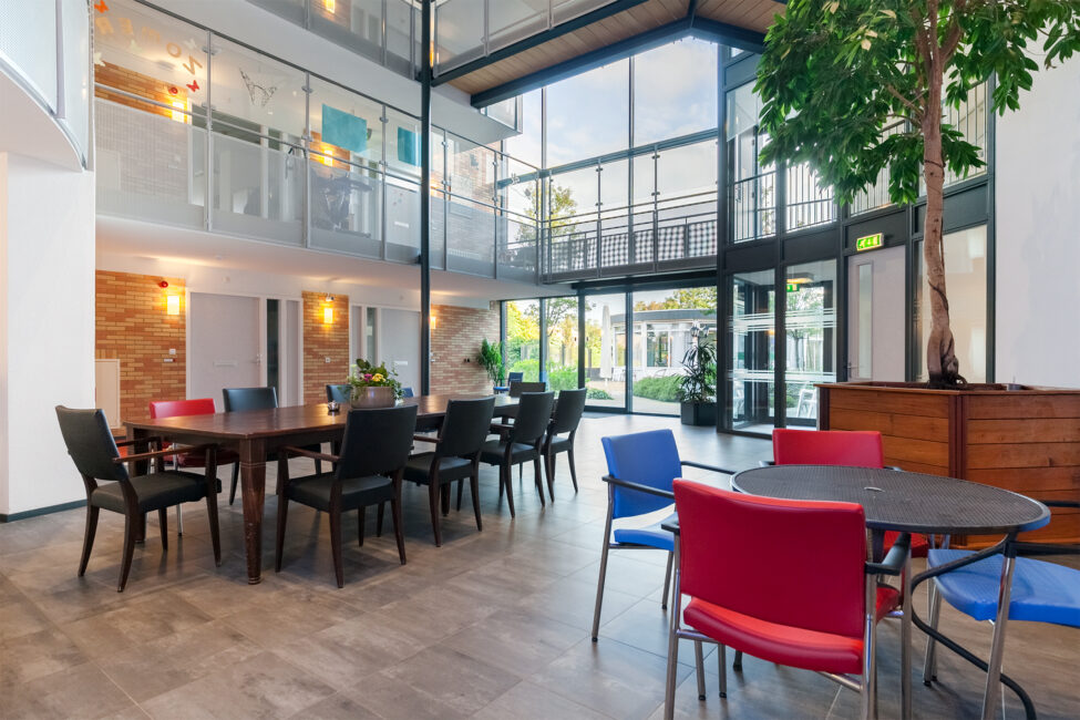Interieur van een moderne gemeenschappelijke ruimte met tafels, stoelen en veel natuurlijk licht door grote ramen.