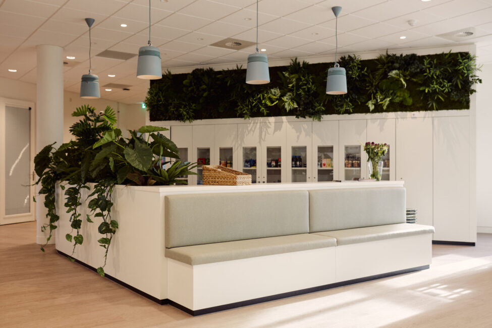 Moderne wachtkamer met witte banken, groene plantenwand en hanglampen. Rustige sfeer met veel natuurlijke elementen.
