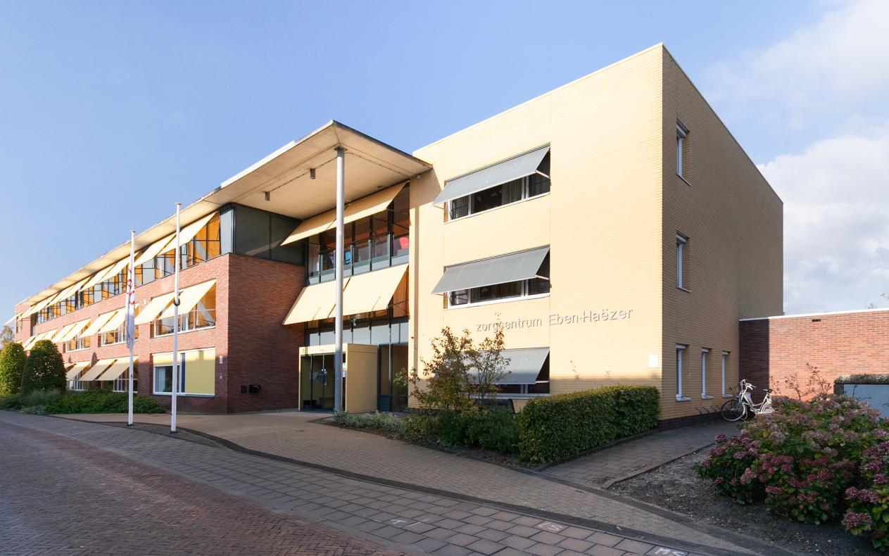 Afbeelding van een modern gebouw met meerdere verdiepingen, grote ramen en zonwering, gelegen aan een rustige straat.