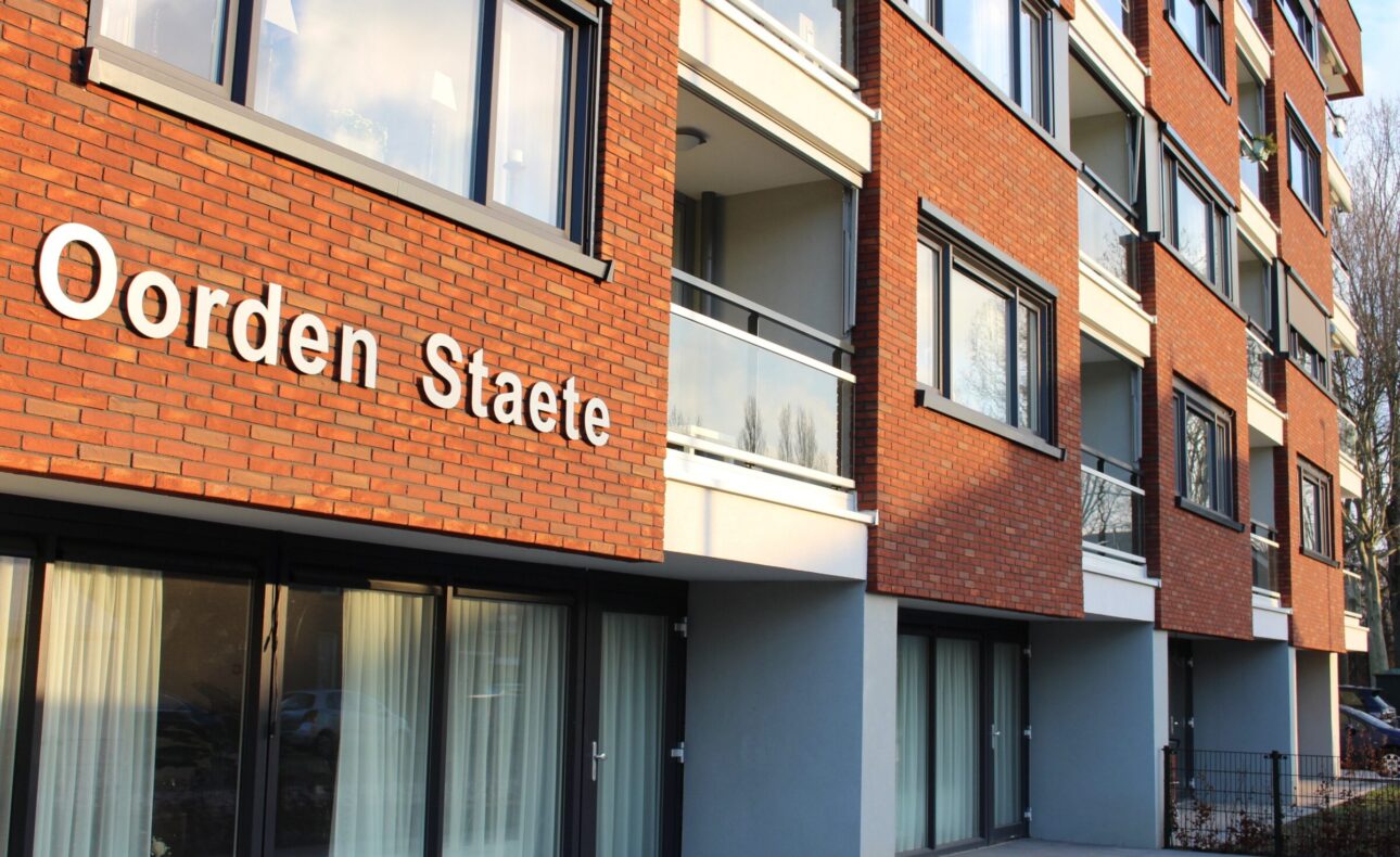Afbeelding van de buitenkant van een modern appartementencomplex met de naam "Oorden Staete" op de gevel.