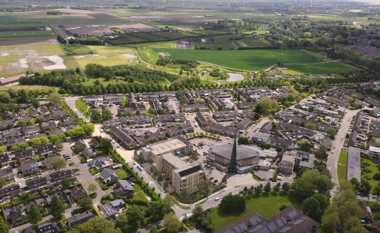 Luchtfoto van een groene woonwijk met huizen, wegen en bomen, omringd door velden en een park in de verte.