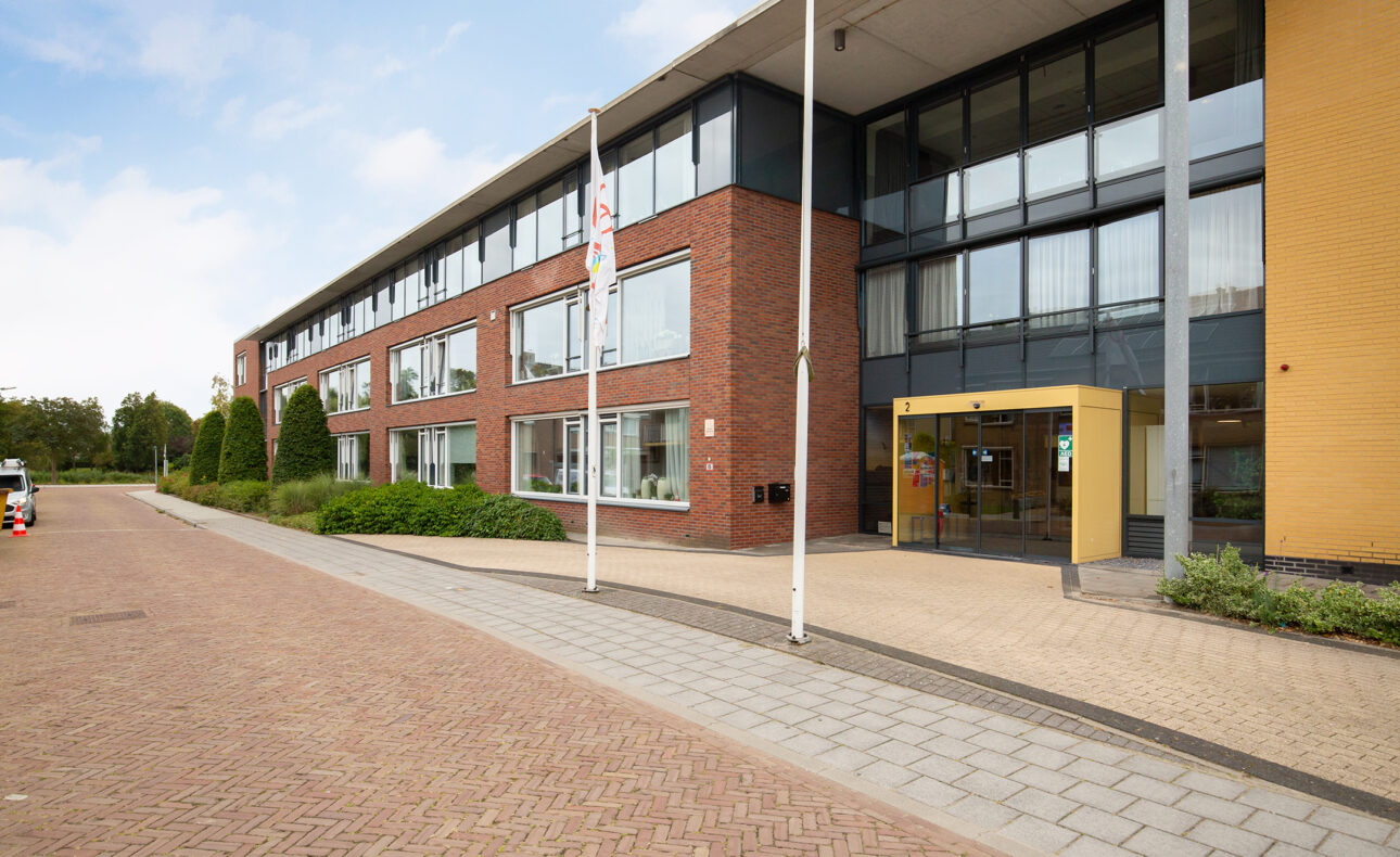 Buitenaanzicht van een modern gebouw met bakstenen en glazen gevel, omgeven door een stoep en een rustige straat.