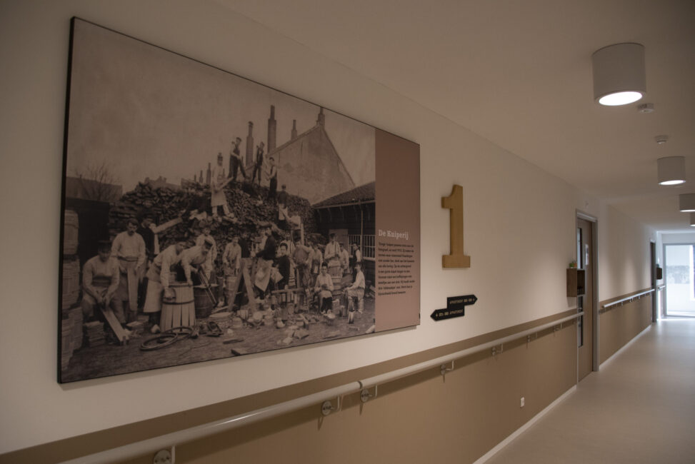 Gang in een gebouw met een grote zwart-witfoto aan de muur. Er hangt een bord met het nummer één naast de foto.