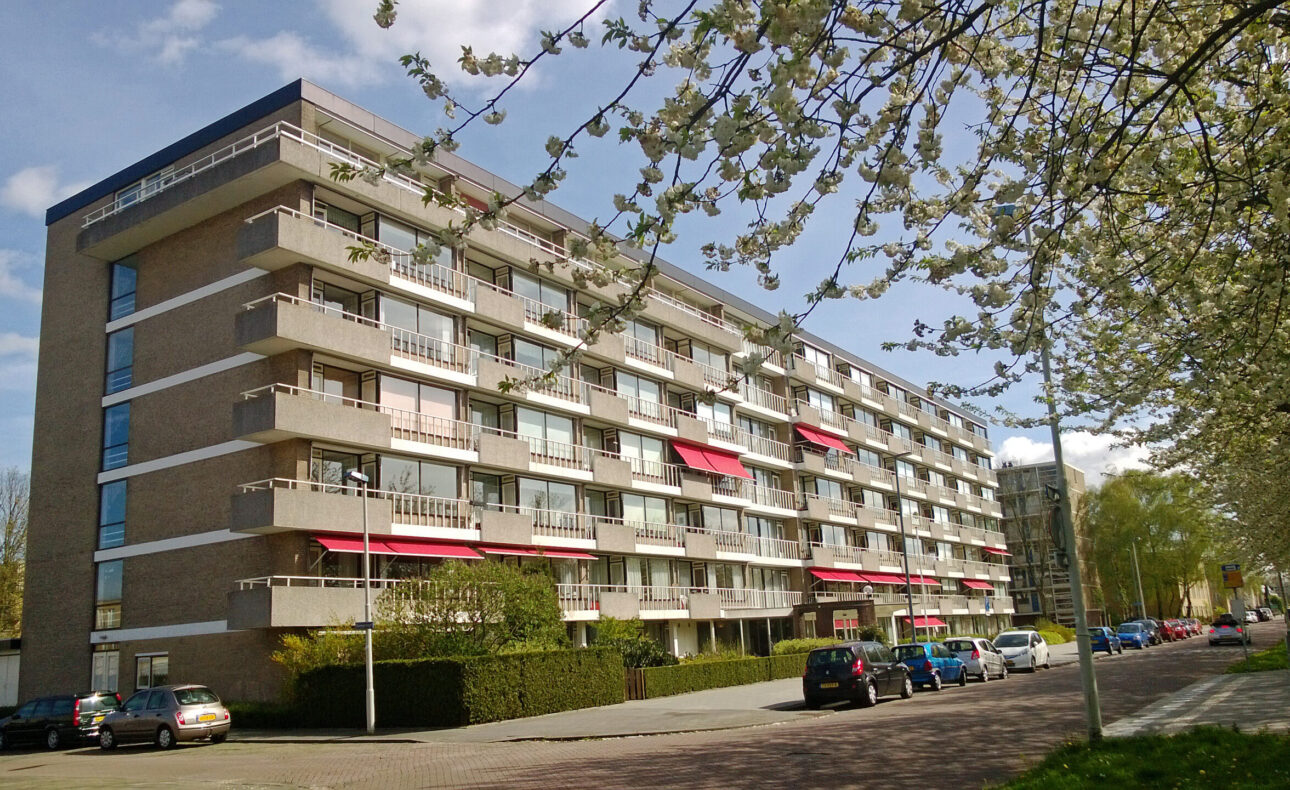 Appartementencomplex met zes verdiepingen in Rotterdam, omgeven door bomen en geparkeerde auto's langs de straat.