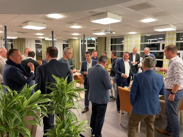 Een groep mensen in een kantooromgeving, gekleed in zakelijke kleding, staat in een kring en voert een gesprek.