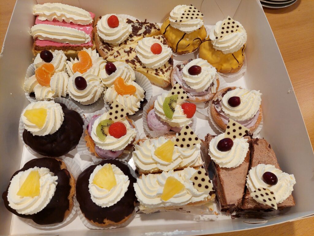 Een doos met diverse gebakjes, waaronder taartjes met slagroom, fruit en chocolade, op een houten tafel gepresenteerd.