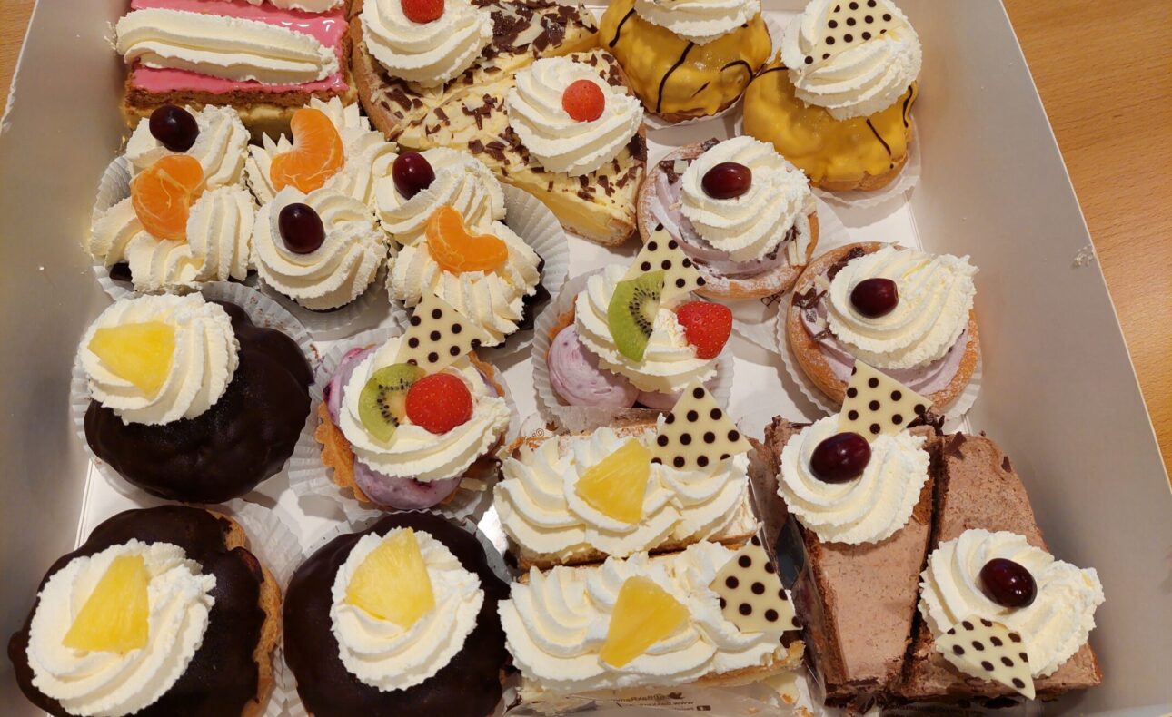 Een doos met diverse gebakjes, waaronder taartjes met slagroom, fruit en chocolade, op een houten tafel gepresenteerd.