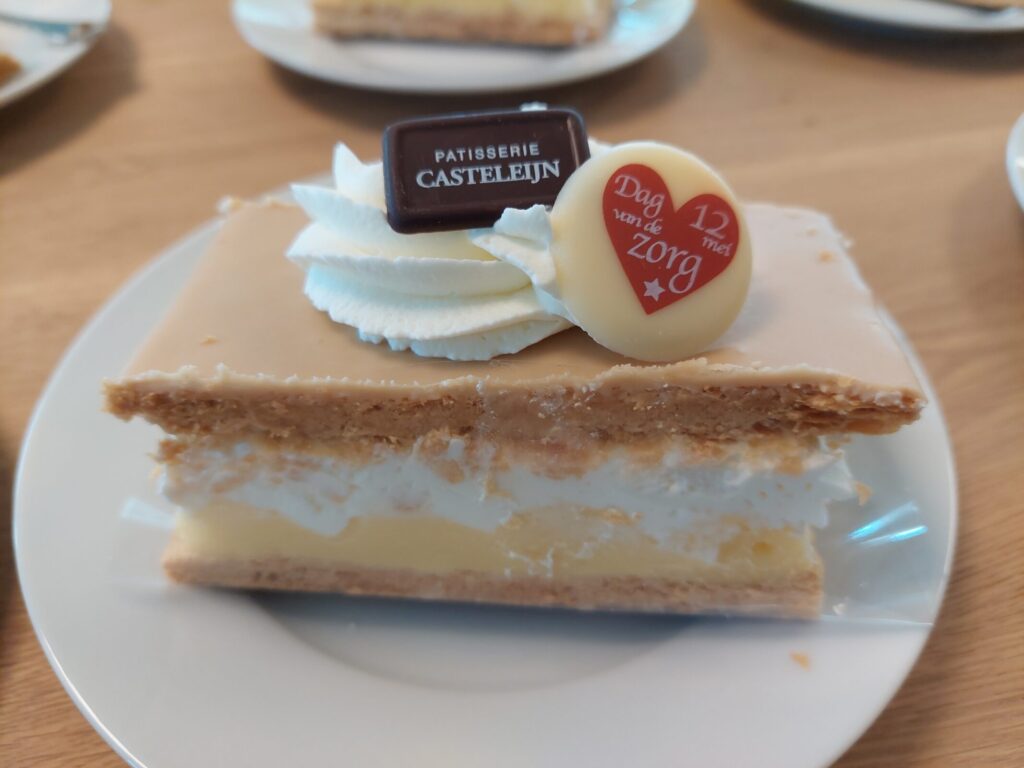 Een gebakje met room en een laagje chocolade, versierd met slagroom en een logo van Patisserie Castelijn op een bord.