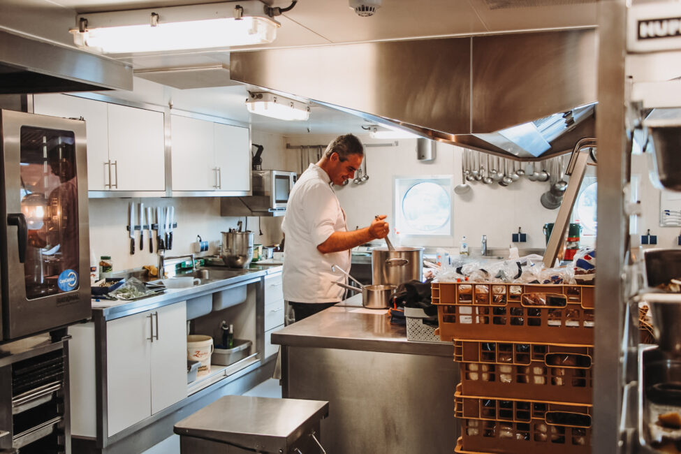 Een kok bereidt een gerecht in een professionele keuken, omringd door keukengerei en ingrediënten op het aanrecht.