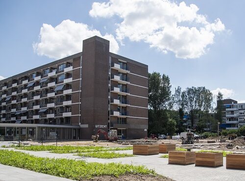 Afbeelding van een modern, zes verdiepingen hoog gebouw met balkons, omgeven door een groen landschap en blauwe lucht.
