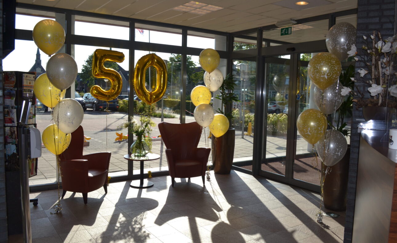 Twee stoelen in een zonnige ruimte met gouden en witte ballonnen. Grote gouden ballonnen vormen het getal 50.