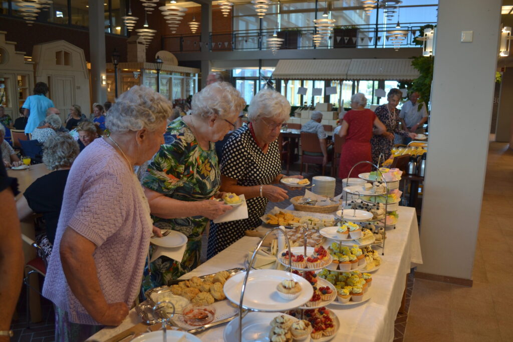 Oudere dames kiezen hapjes van een buffet in een gezellige eetzaal met veel licht en een moderne inrichting.