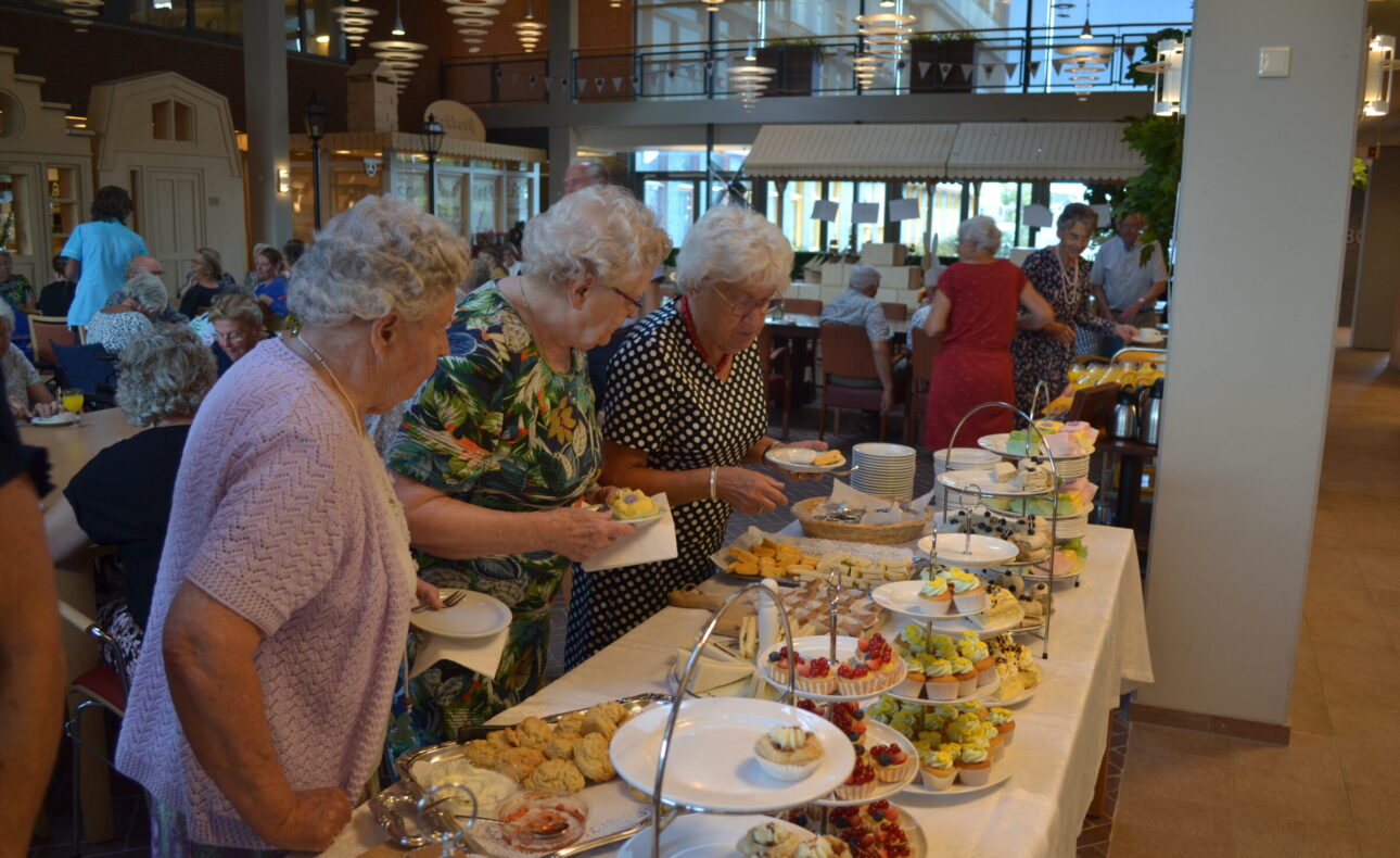 Oudere dames kiezen hapjes van een buffet in een gezellige eetzaal met veel licht en een moderne inrichting.