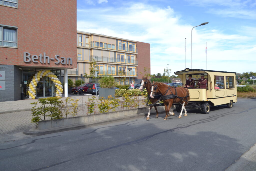 Paard en wagen voor de ingang van een gebouw met de naam "Beth-San". Het is een zonnige dag met een blauwe lucht.