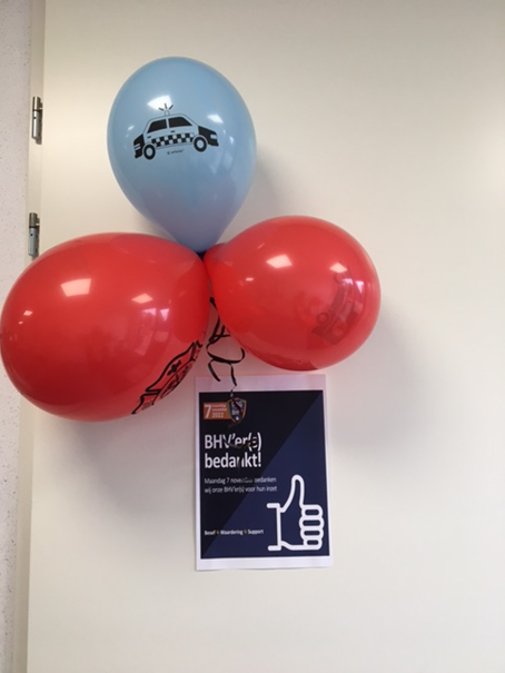 Drie ballonnen in rood en blauw zijn aan een deur bevestigd, met daaronder een poster met een duim omhoog symbool.