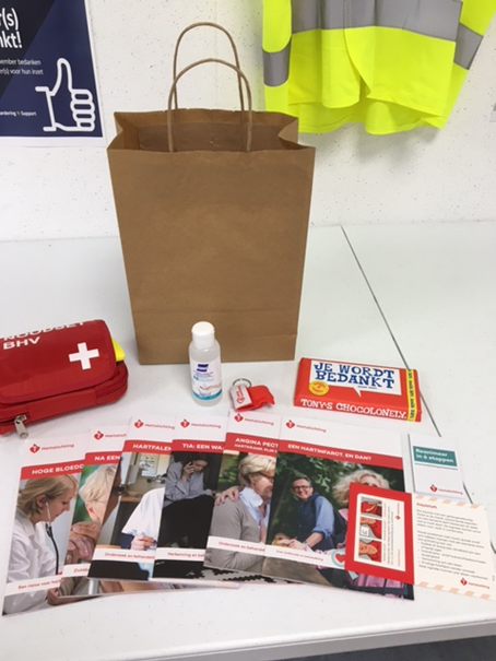 Een papieren tas met EHBO-set, ontsmettingsmiddel, chocoladereep en folders over zorg en veiligheid op een tafel.