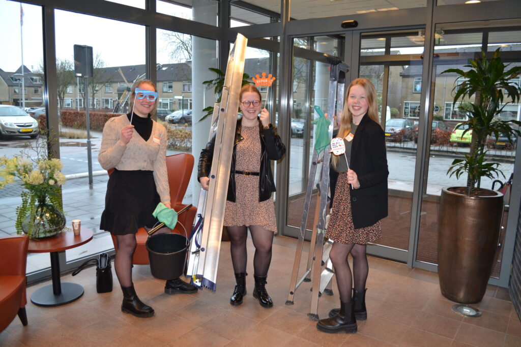 Drie vrouwen staan in een entreehal met schoonmaakspullen en ladders, klaar om te beginnen met schoonmaken.