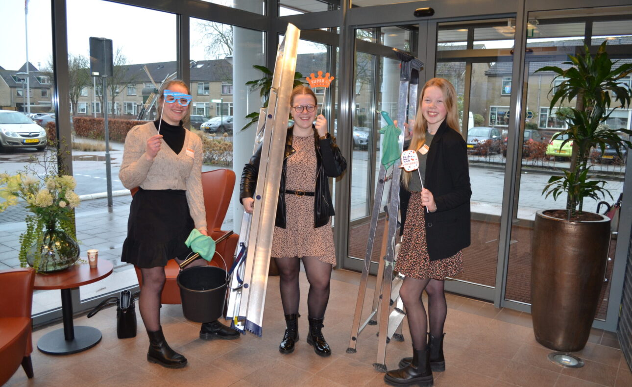 Drie vrouwen staan in een entreehal met schoonmaakspullen en ladders, klaar om te beginnen met schoonmaken.