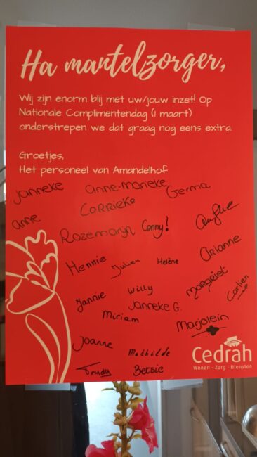 Poster met de tekst "Ha mantelzorger" en handtekeningen van medewerkers, met een rode achtergrond en witte bloemen.