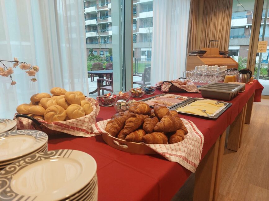 Ontbijtbuffet met croissants, broodjes, kaas en vleeswaren op een tafel met rood tafelkleed, klaar voor de Dag van de Zorg.