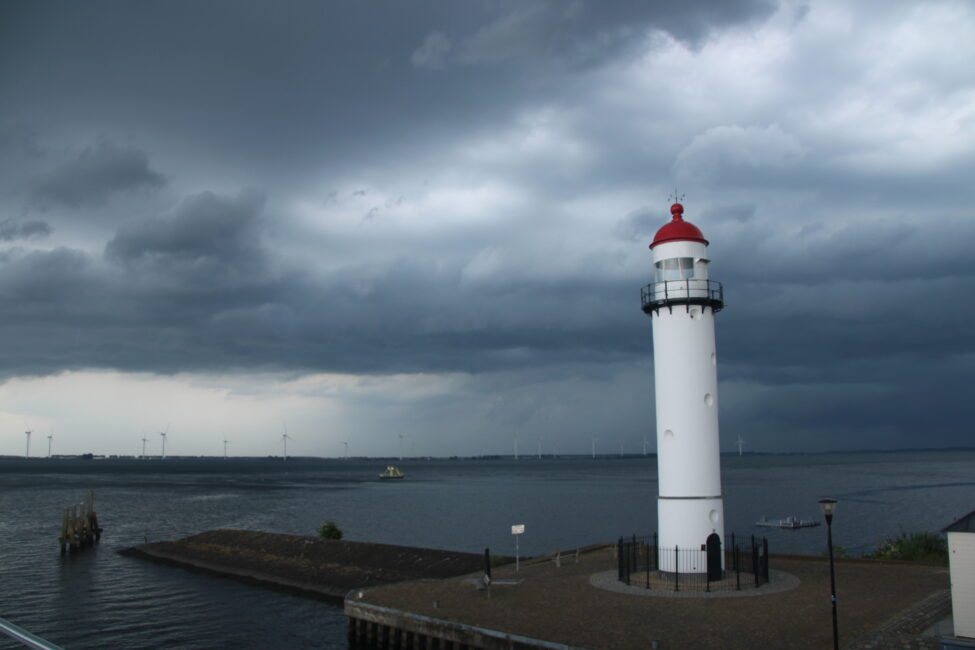 Vuurtoren aan de kust onder een dreigende, bewolkte hemel. De zee is kalm en de horizon is donker door naderende storm.