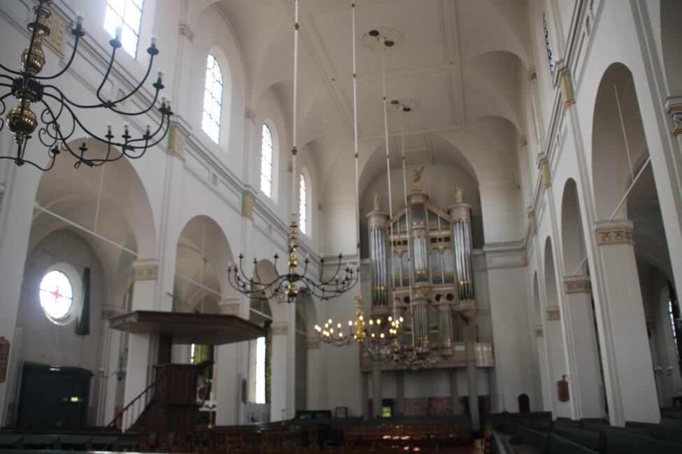 Interieur van een historische kerk met hoge gewelfde plafonds, grote kroonluchters en een indrukwekkend pijporgel.