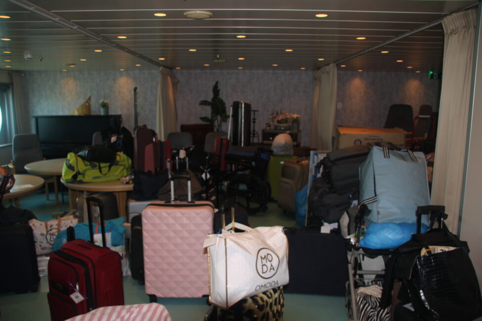 Stapel koffers en tassen in een kamer met zachte verlichting en zitgedeelte. Verschillende kleuren en maten bagage zijn zichtbaar.