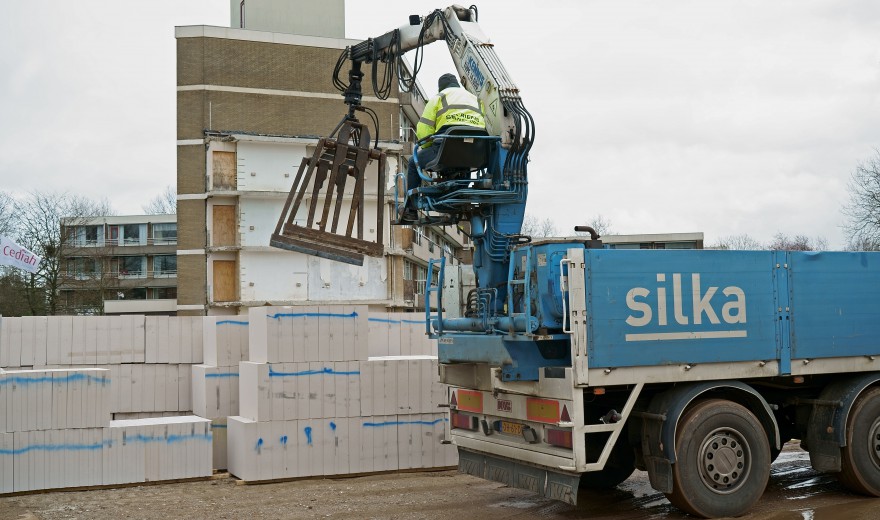 Een bouwvakker bedient een kraan op een vrachtwagen om bouwmaterialen te verplaatsen bij een bouwplaats met stapels stenen.