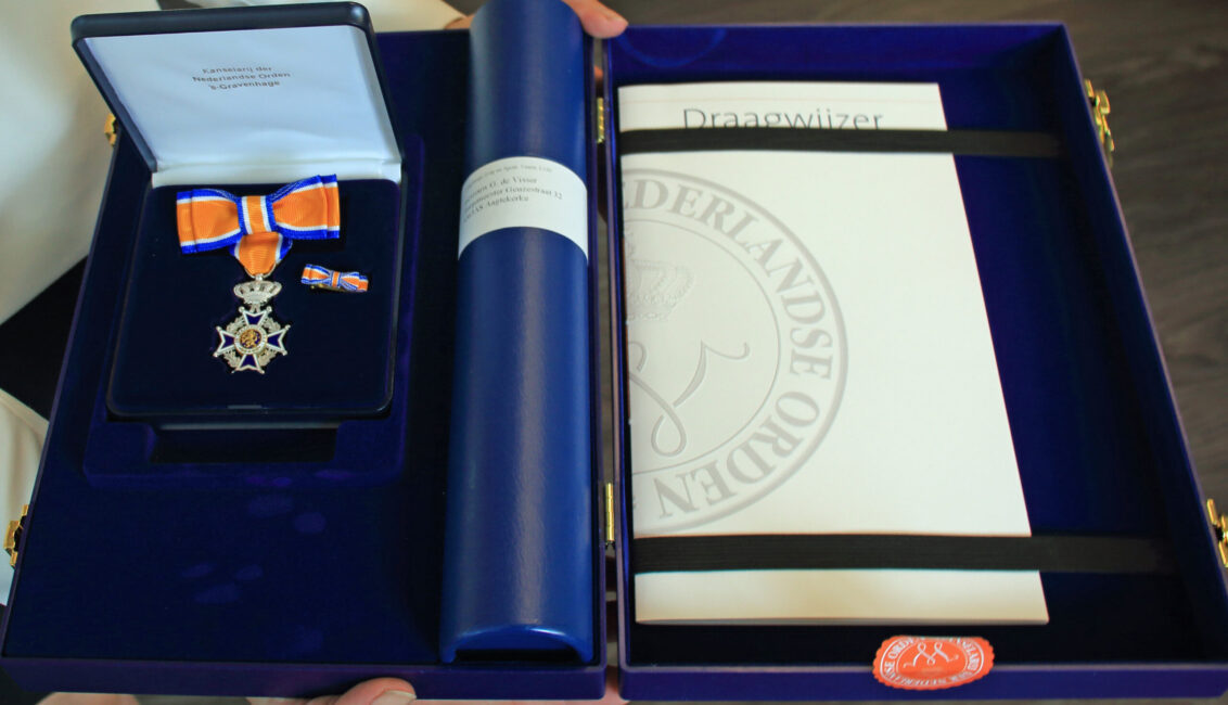 Een koninklijke onderscheiding in een blauwe doos, met een lint, medaille en certificaat van de Nederlandse Orde van Oranje-Nassau.