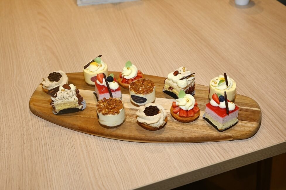 Een houten plank met een assortiment van kleurrijke mini-desserts, waaronder taartjes met fruit, chocolade en room, op een tafel.
