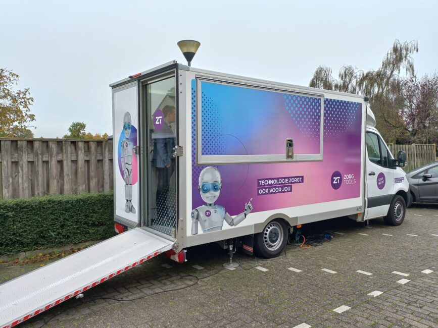 Een kleurrijke mobiele unit met een robotillustratie op de zijkant, geparkeerd op een parkeerplaats met een uitgeschoven oprijplaat.
