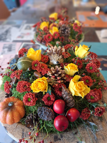 Herfststuk met gele rozen, rode bloemen, dennenappels, pompoen en rode bessen op een houten tafel. Sfeervol en kleurrijk.