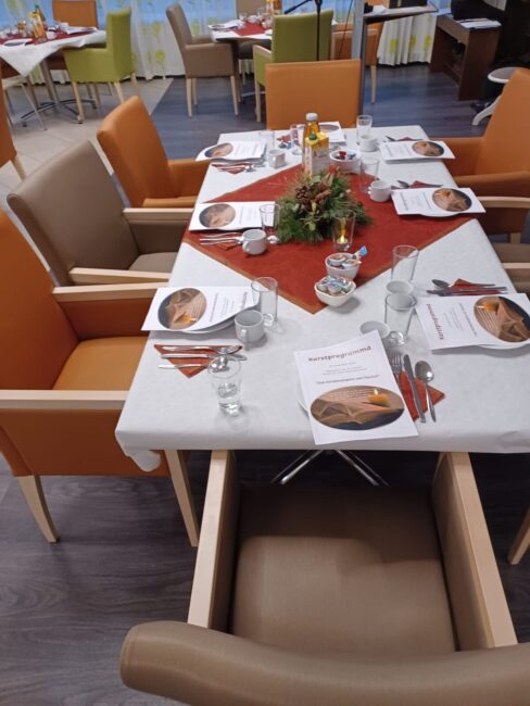 Een feestelijk gedekte tafel met oranje en beige stoelen, servetten, menukaarten en een bloemstuk in een eetzaal.