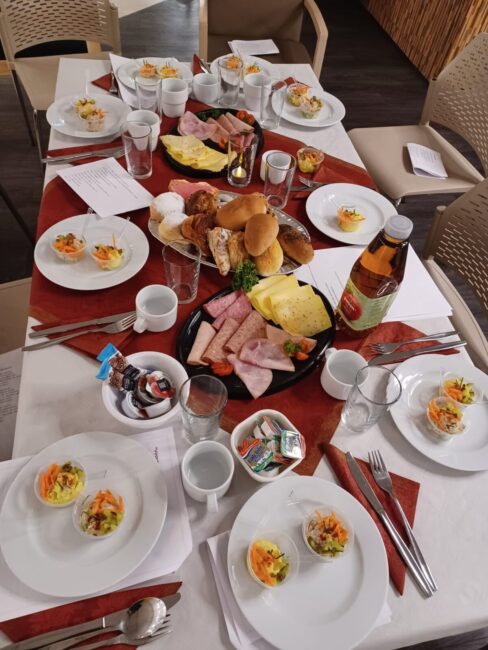 Een gedekte tafel met diverse ontbijtproducten zoals broodjes, vleeswaren, eieren en drankjes, klaar voor een gezamenlijke maaltijd.