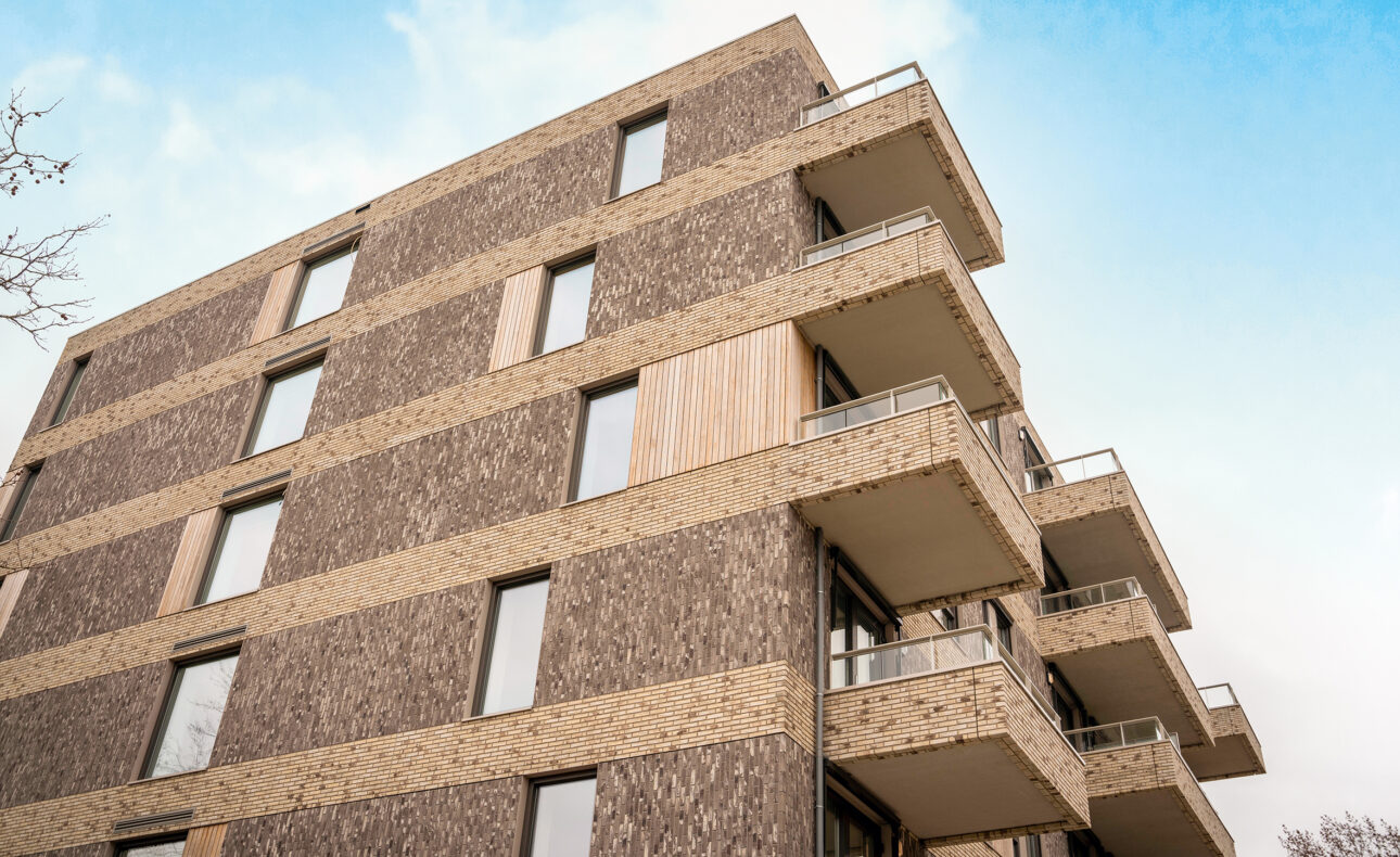 Afbeelding van een modern appartementencomplex met bakstenen gevels en meerdere balkons, gefotografeerd vanuit een laag perspectief.