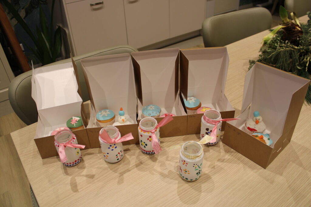 Een tafel met versierde cupcakes in open dozen en glazen potjes met roze linten, klaar voor een feestelijke gelegenheid.