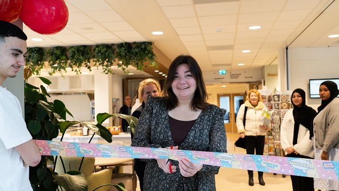 Een vrouw knipt een lint door tijdens een openingsceremonie in een modern ingerichte ruimte, omringd door toeschouwers.