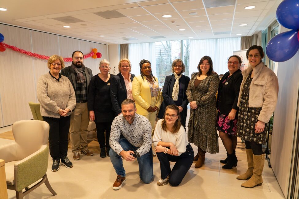 Groep mensen poseert samen in een lichte kamer met feestelijke decoraties, zoals ballonnen en slingers, op de achtergrond.