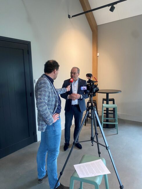 Twee mannen in gesprek tijdens een mediatraining. Een man houdt een microfoon vast, terwijl de ander voor een camera staat.