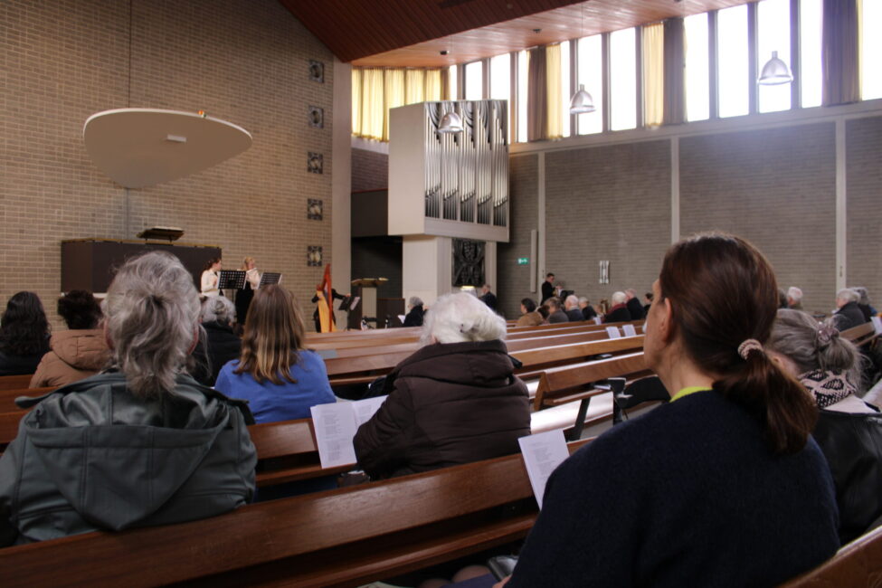 Mensen zitten in kerkbanken tijdens een kerkdienst. Ze luisteren aandachtig naar de spreker voorin de moderne kerk.