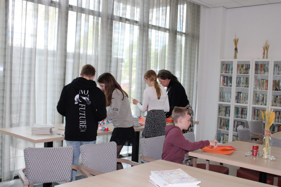 Een groep mensen werkt samen aan een tafel in een lichte ruimte met grote ramen en een boekenkast op de achtergrond.