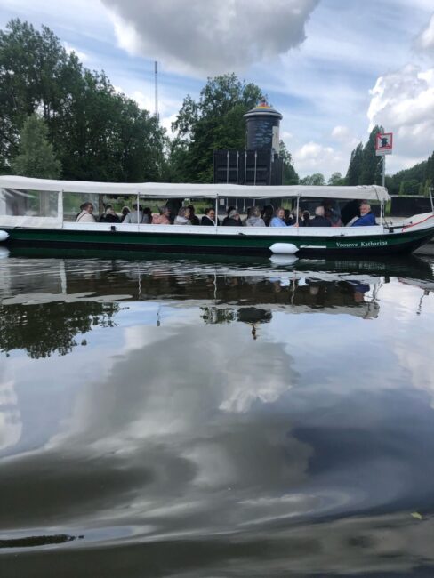 Een groep mensen geniet van een boottocht op een rustige rivier, omringd door groene bomen en een bewolkte hemel.