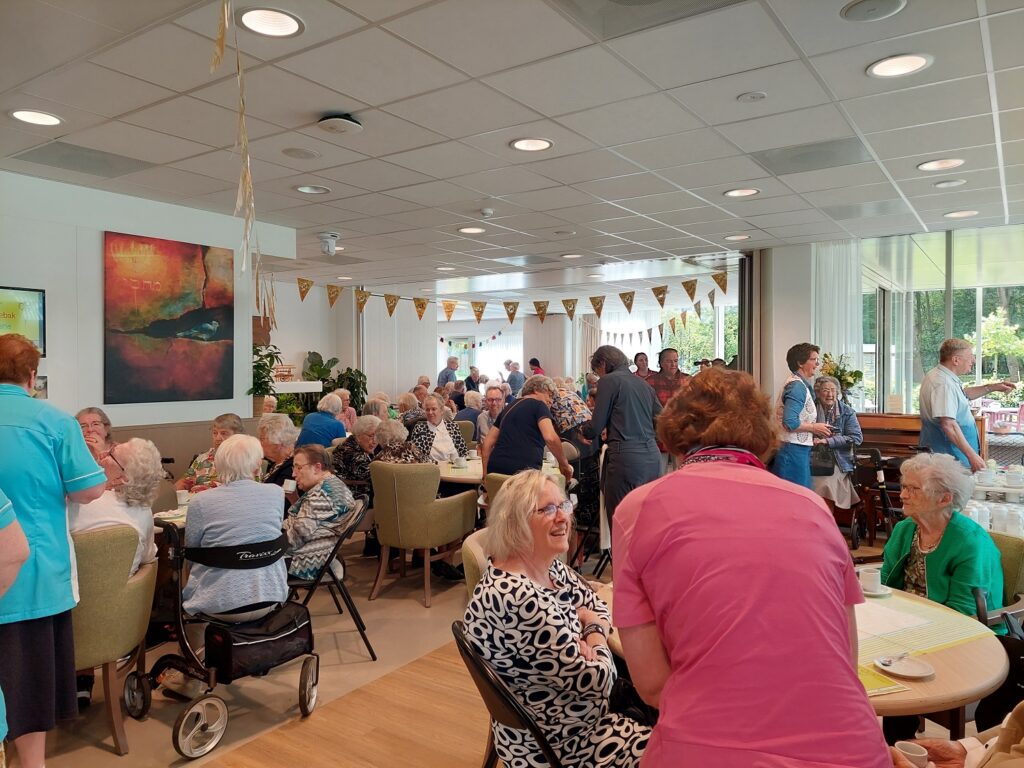 Groep mensen viert een feestelijke dag in een gemeenschappelijke ruimte met slingers en schilderijen aan de muur.